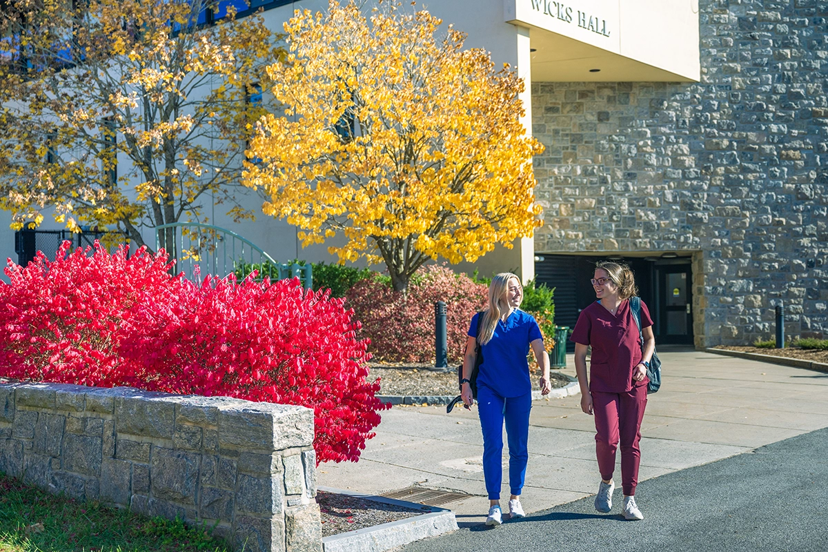 Two nursing students walk outside Wicks Hall on a beautiful autumn day.