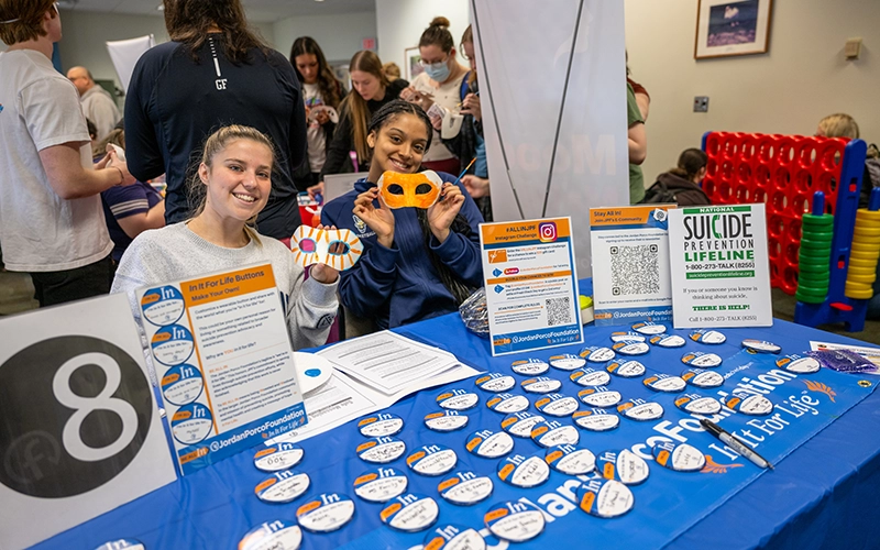 Two students hold up custom masks while sitting at a suicide prevention table during Fresh Check 2025.