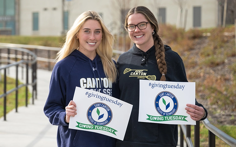 Two students hold Giving Tuesday signs outside French Hall.