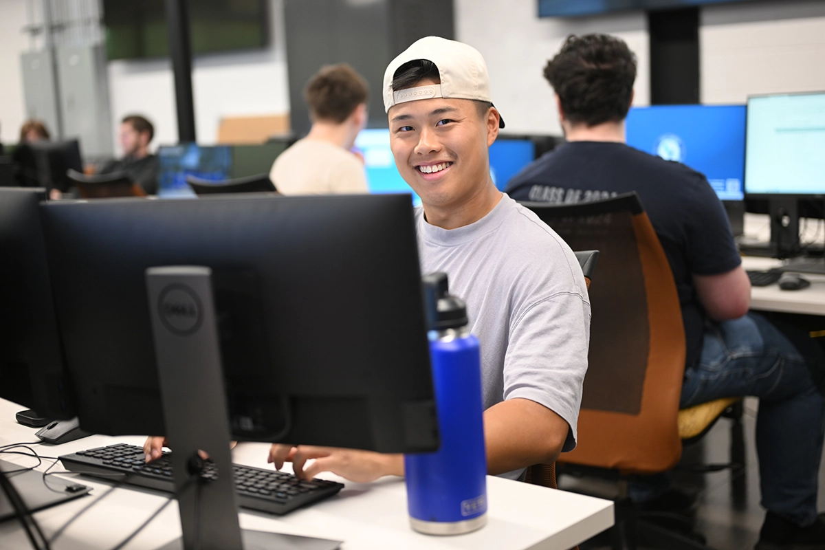 A student smiles from behind a computer in the Information Technology Lab.