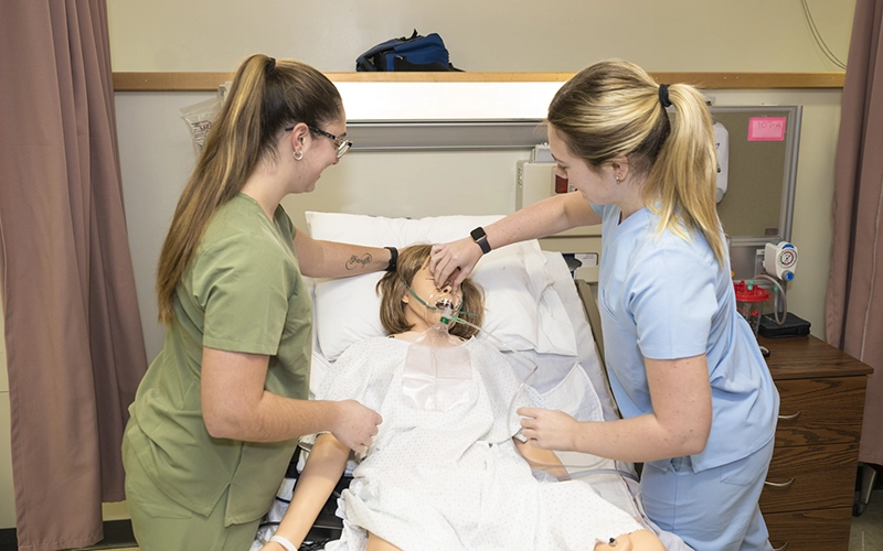 Two nursing students work with a model patient in the Nursing Simulation lab.