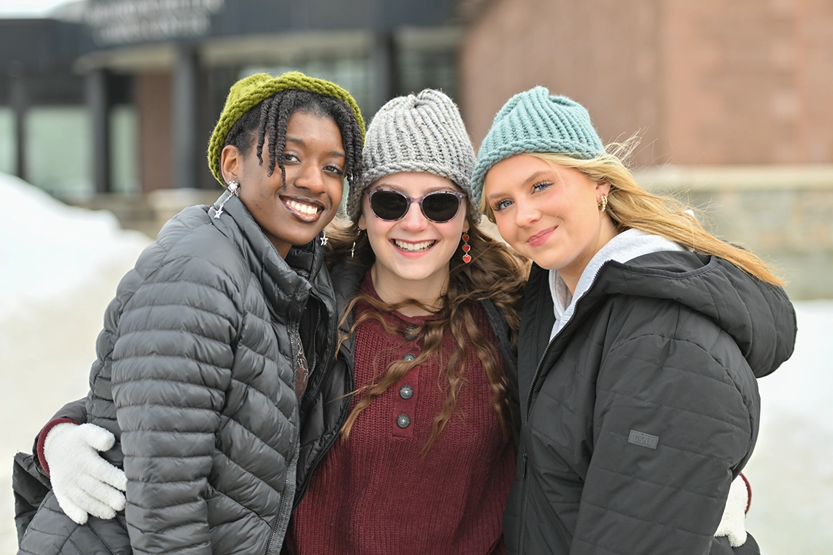 Three students wearing food pantry-donated knit hats outside the Miller Campus Center.