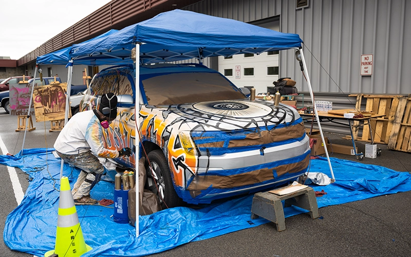 Docta spray paints an SUV outside SUNY Canton's Automotive Lab.