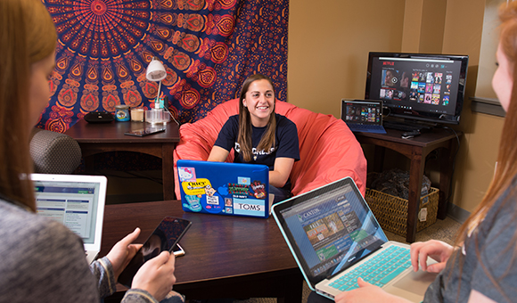 Three students view laptops in their residence hall.