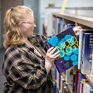 A student takes a Micro Biology textbook off a shelf at Southworth Library.