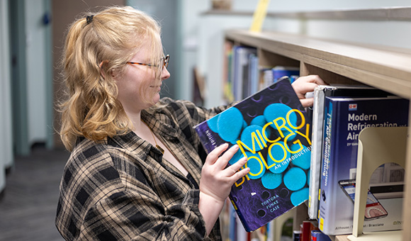 A student takes a Micro Biology textbook off a shelf at Southworth Library.