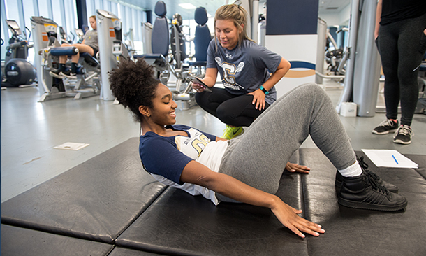 A student trains another how to do sit-ups in the Fitness Center