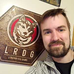 Ryan Hewer poses in front of a Little Red Dog Gaming logo