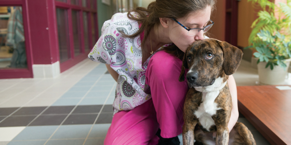 A veterinary student hugs and kisses a dog.