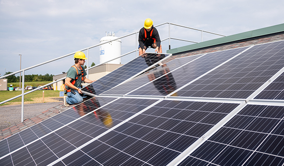 Electrical Construction and Maintenance students Gregory Sthilaire and Daniel Manor installing solar panels on the college's solar roof simulator.