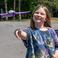 A camper flies a purple foam glider outdoors.
