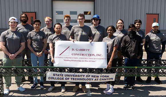 Steel Bridge team holding banner in front of Nevaldine Hall.