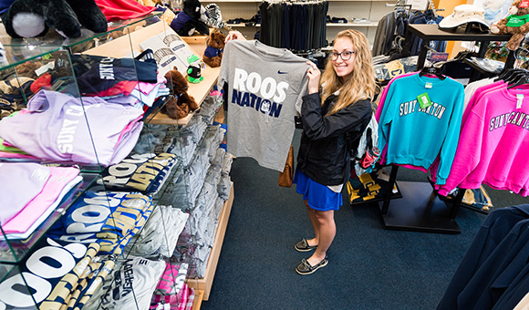 A student holds up a gray Roos Nation T-shirt at the Campus Store