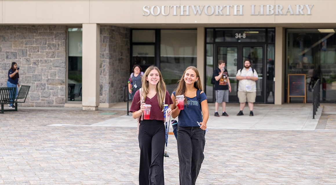 Two students enjoy iced Starbucks drinks as they depart Southworth Library.