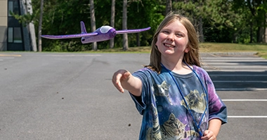 A camper flies a purple model airplane outside.