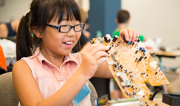 A young student works on a motherboard at summer camp.