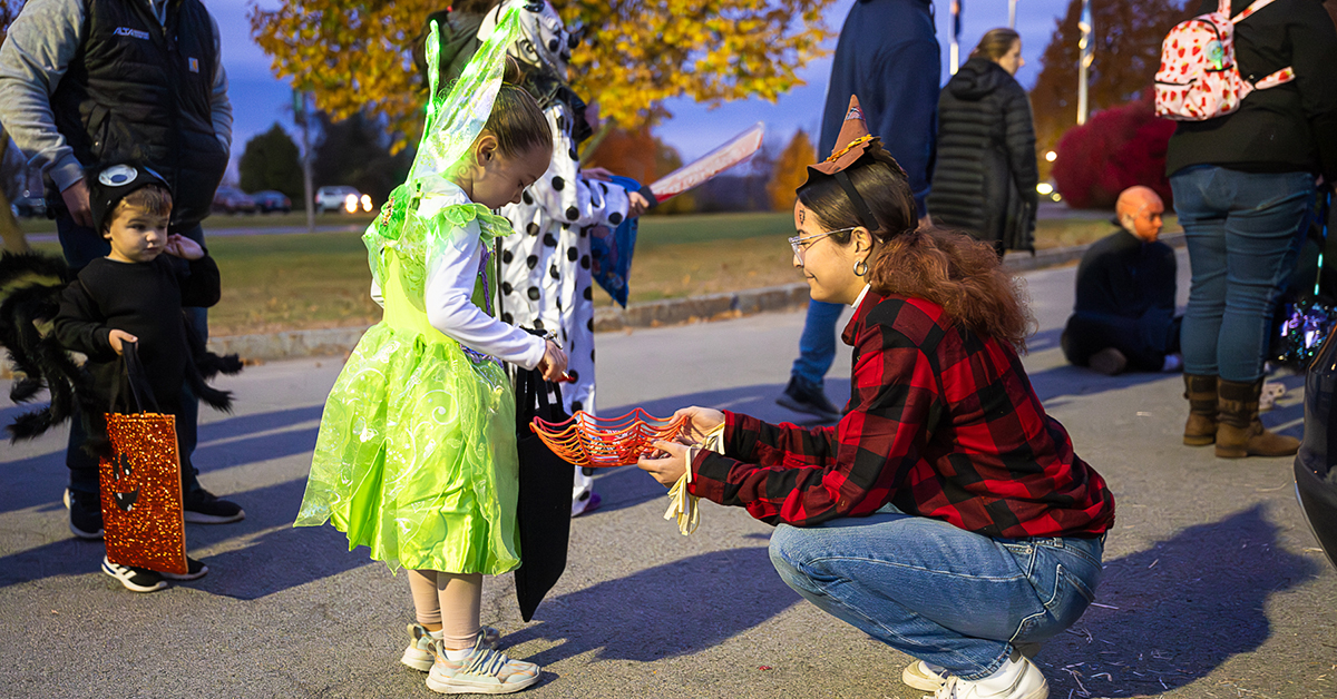 A girl dressed in a neon green fairy costume selects candy from a SUNY Canton student's bowl.