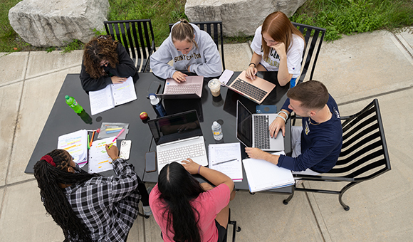 Students working on laptops on a table outside Dana Hall