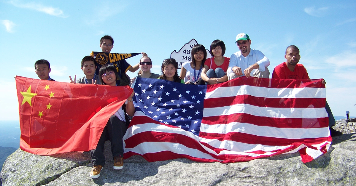 Chinese exchange students hold Chinese and US flags on top of Whiteface Mountain.