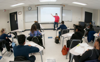 A professor lectures to a class full of students.